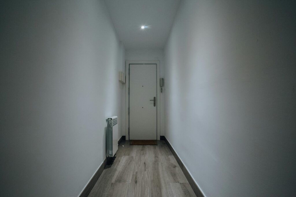 A simple and clean indoor hallway featuring a closed door and wooden flooring.