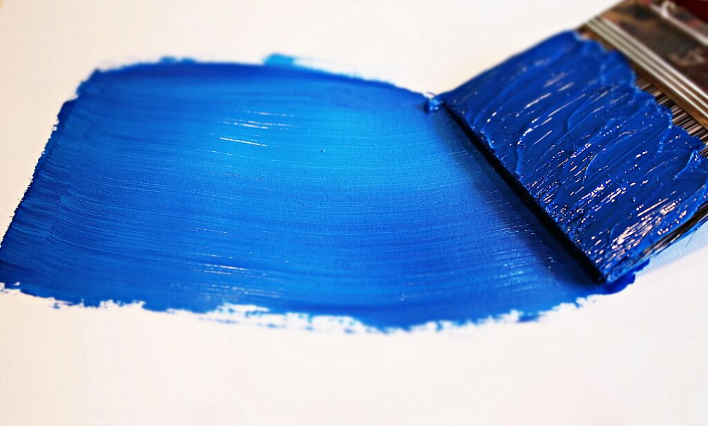 Close-up of a vivid blue brushstroke applied to a white canvas using a paintbrush.